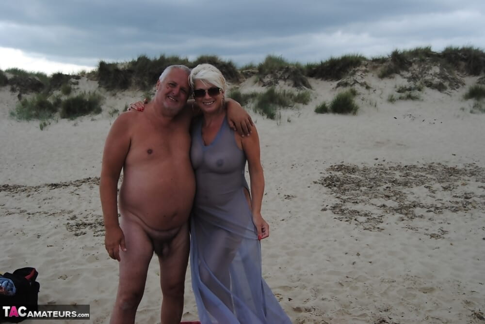 Mature blonde Dimonty eats a frozen treat after posing nude on a beach