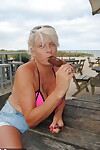 Mature blonde Dimonty eats a frozen treat after posing nude on a beach
